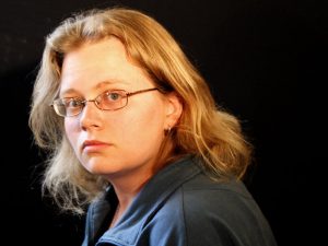 Headshot of Seanan, a white woman with mid-length blond hair, wearing glasses and a blue collared blouse